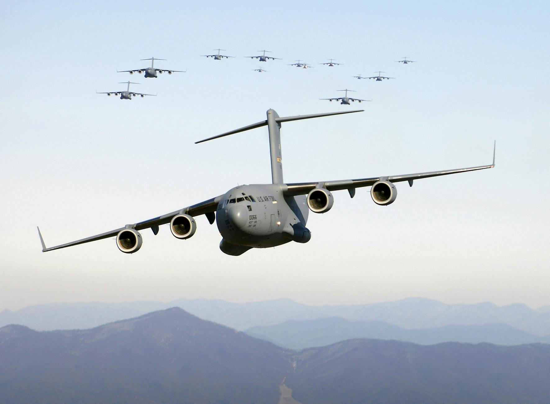 A formation of military cargo aircraft flying over a mountainous landscape, showcasing aviation power.